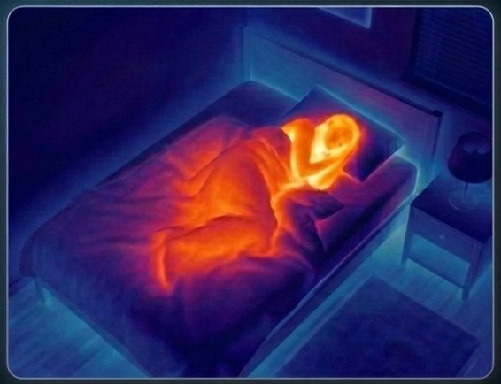 Thermal-sensor view of a person resting in bed — ironbow filter, no identifiable detail.